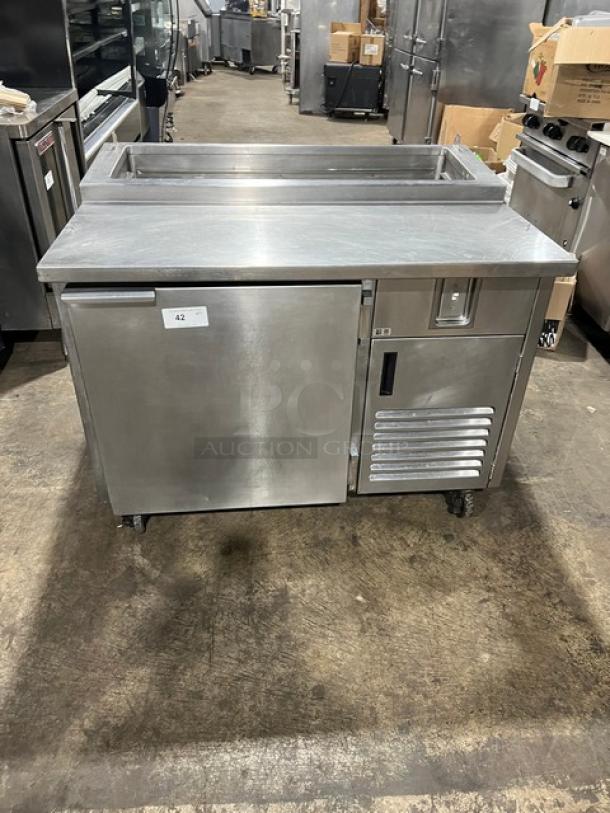 Commercial stainless steel refrigerated pizza prep table with single door, chrome-plated wired rack, and casters.