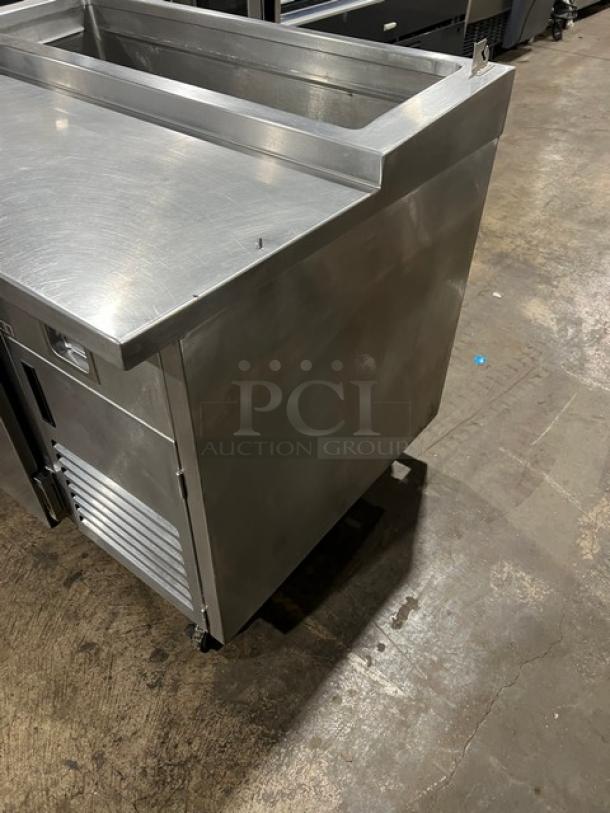 Commercial stainless steel refrigerated pizza prep table with a single door, chrome-plated rack, and casters.