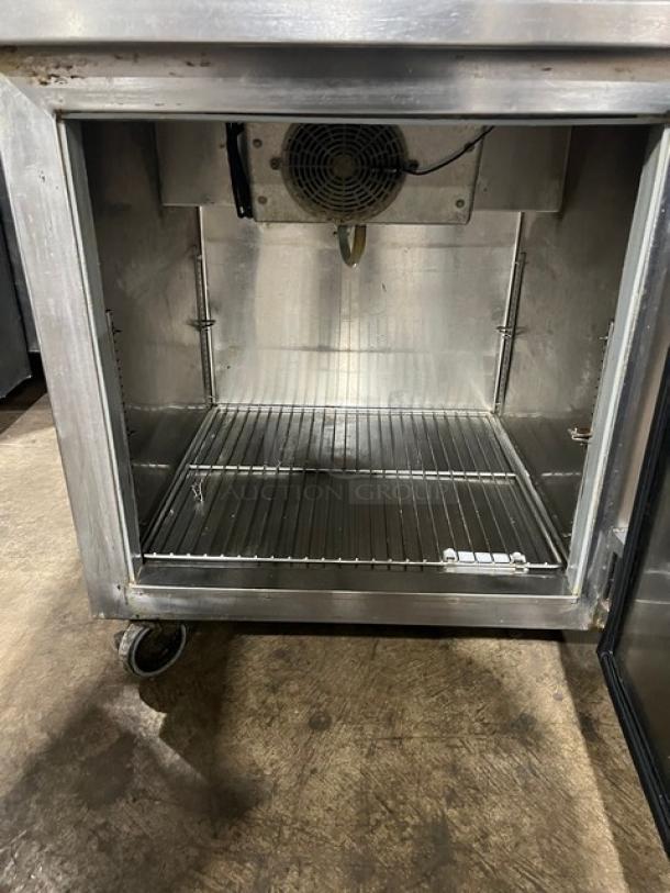 Commercial stainless steel single door pizza prep table with chrome-plated wire rack, on casters, open door view.