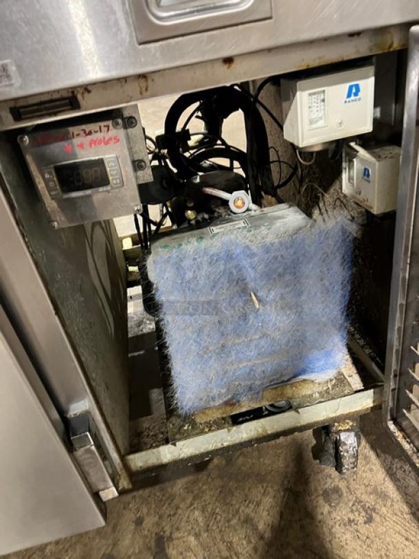 Commercial stainless steel refrigerated pizza prep table with single door, chrome-plated rack, on casters, visible interior components.