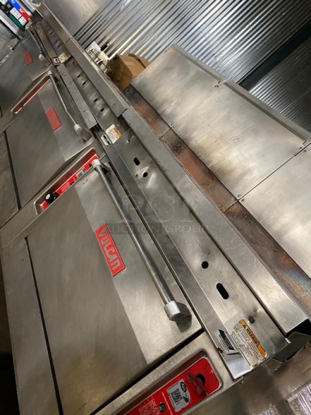 Vulcan stainless steel gas 8-burner range with split-top griddle, triple oven combo, backsplash, and wired oven rack on casters.