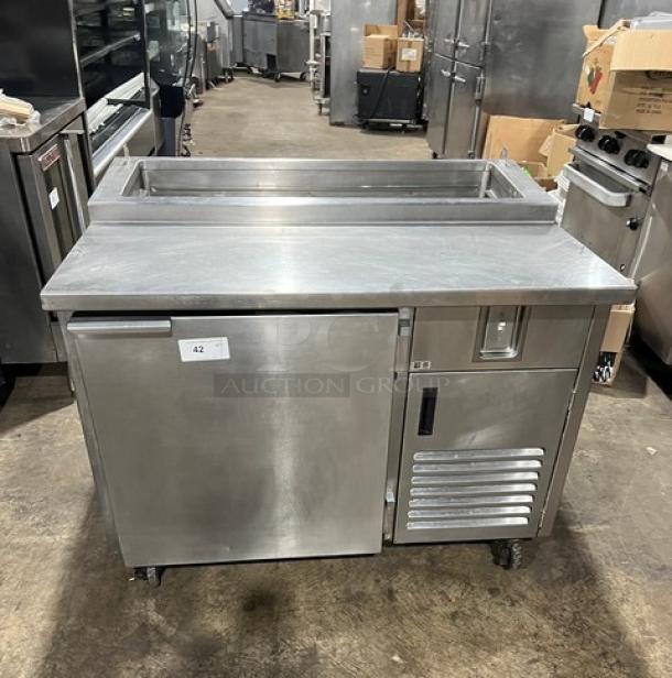 Commercial stainless steel refrigerated pizza prep table with single door, chrome-plated wired rack, and casters.