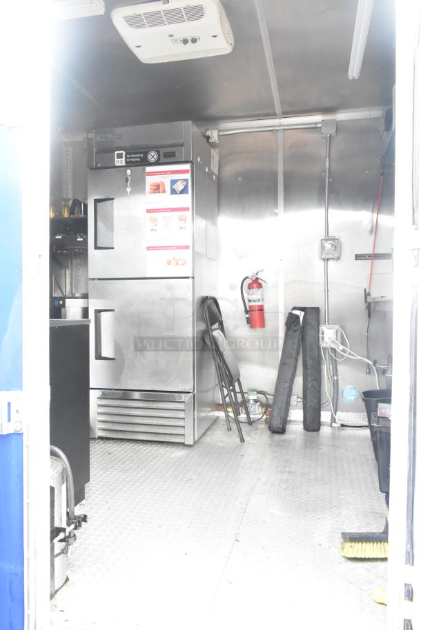 Cruising Kitchens 24' fast food trailer interior with stainless steel True reach-in cooler, CaptiveAire grease hood, and fire extinguisher.