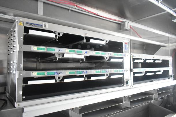 Interior view of a Cruising Kitchens 24' mobile food trailer featuring commercial-grade equipment, including cooling racks and metal shelving, in excellent condition.