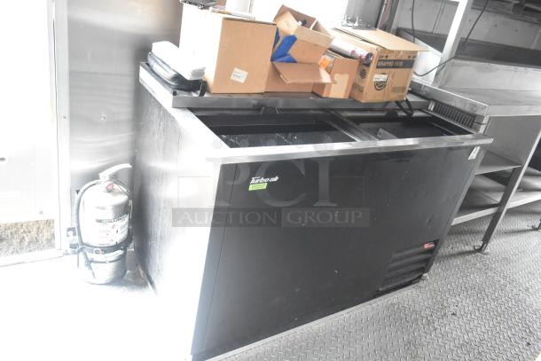 Cruising Kitchens 24' food trailer interior with Turbo Air cooler, boxes, fire extinguisher, and stainless steel shelves.