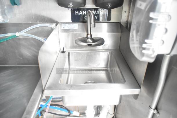 Stainless steel hand sink with motion sensor faucet, marked "Hand Wash Only," in mobile kitchen trailer.