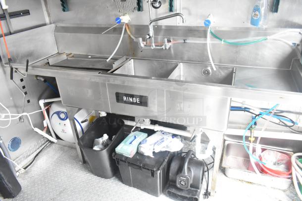 Stainless steel kitchen sink setup in a 2021 Cruising Kitchens fast food trailer. Features "RINSE" label, plumbing, and storage below.