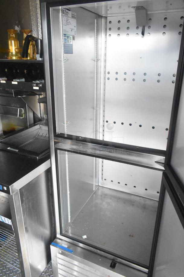 Interior of a mobile kitchen trailer showing a stainless steel True reach-in freezer with empty shelving, visible tags, and sleek design.