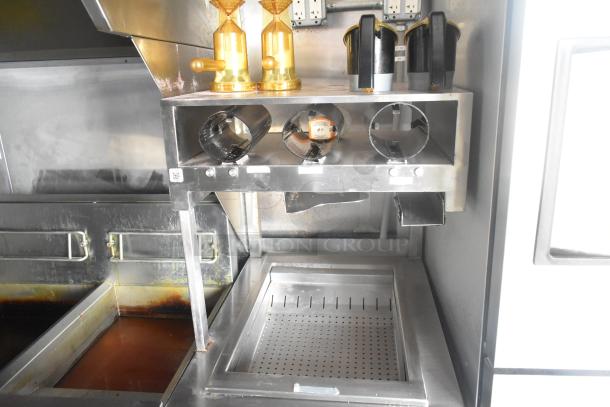 Inside view of a Cruising Kitchens 24' fast food trailer, featuring stainless steel equipment setup including fryers and dispensers.