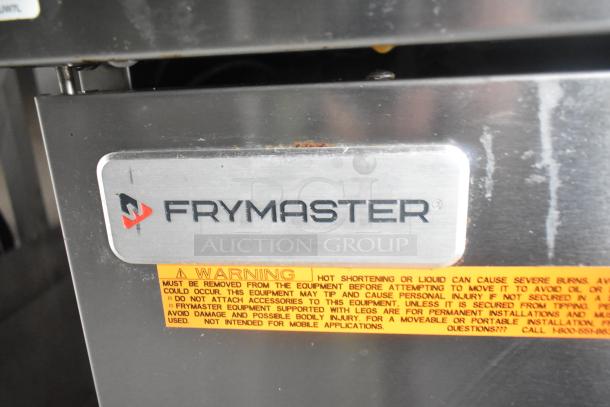 Stainless steel Frymaster gas fryer with visible brand label and safety warning sticker on equipment.