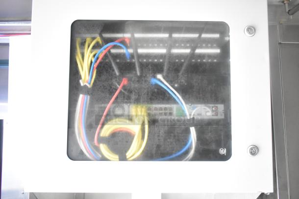 Electrical panel with colored wires visible through a transparent cover, located in Cruising Kitchens' mobile kitchen trailer.