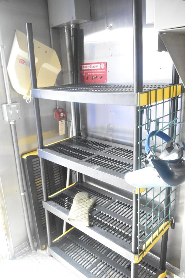 Interior view of a mobile kitchen trailer featuring sturdy metal shelving, safety signage, an oven mitt, and a face shield hanger.