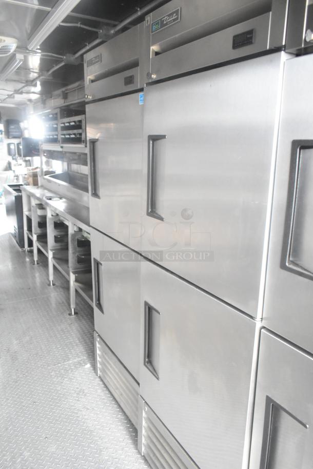 Cruising Kitchens 24' food trailer interior, featuring True reach-in freezers and coolers with stainless steel surfaces.