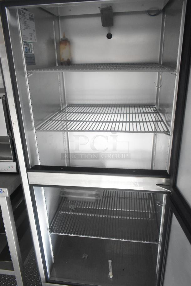 True reach-in cooler with interior wire shelving, shown empty. Features label on the side indicating commercial grade.