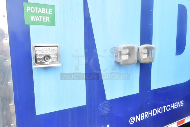 Exterior of a Cruising Kitchens 24' food trailer, featuring a potable water label and two weatherproof electrical outlets.