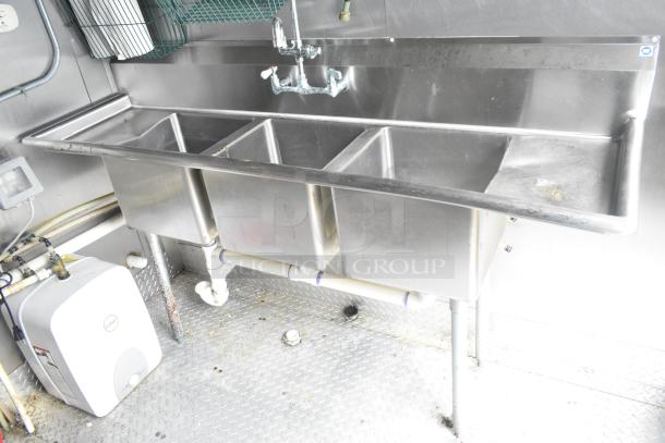 Stainless steel triple sink setup with faucet in an ATX 24' food trailer. Includes under-sink plumbing and water heater.