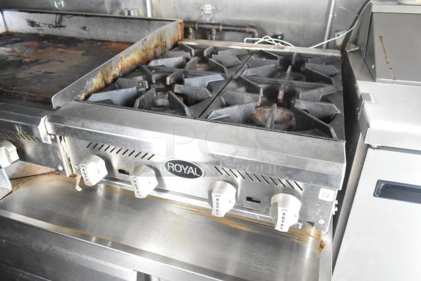 Royal gas range in a food trailer, showing four burners and control knobs. Slight wear on surfaces. Ideal for mobile kitchens.