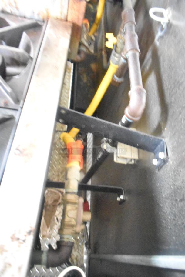 Piping and connections in ATX 24' food trailer showing gas lines, valves, and mounting hardware, indicative of built-in kitchen equipment functionality.