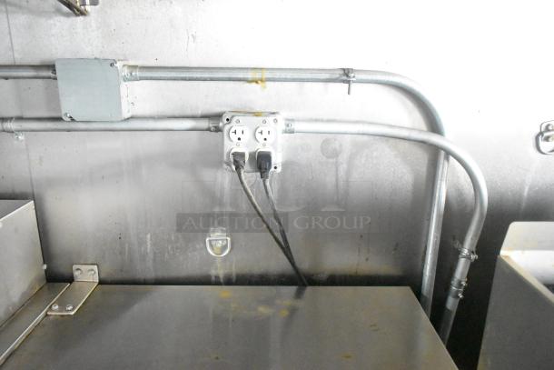 Industrial stainless steel food trailer interior with dual electrical outlet and metal wiring conduits.