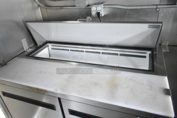 Stainless steel Arctic Air prep table with open lid, showing spacious interior and sturdy design, in a food trailer.