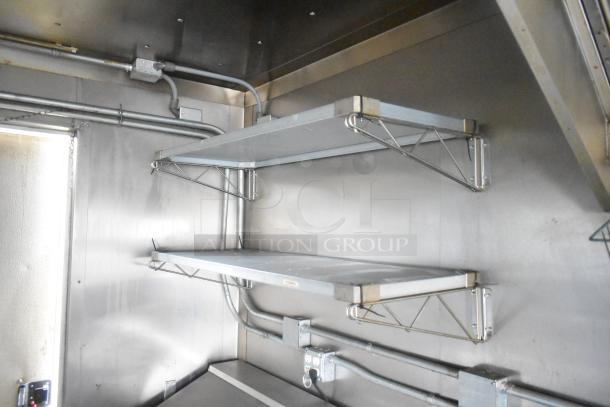 ATX 24' food trailer interior with stainless steel shelves and utility pipes, ready for commercial kitchen use.