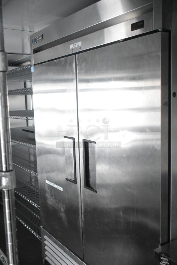 Stainless steel True reach-in cooler with labeled doors for drinks and chocolate candy, wire shelving visible inside.