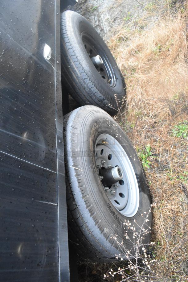Dual wheels of a Southern Dimensions 24' cold food and beverage trailer, showing black exterior and wet weather conditions.