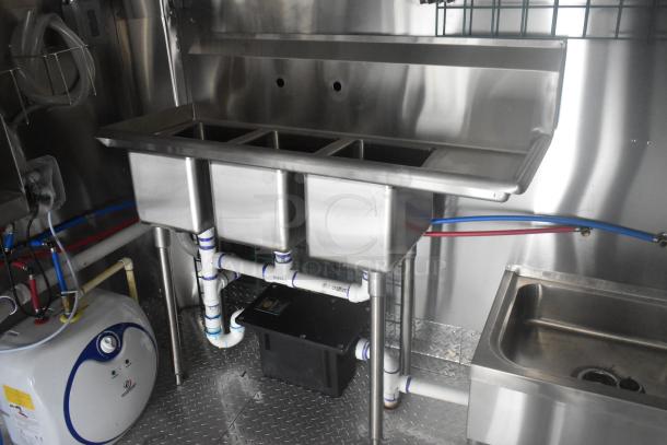 Stainless steel triple sink setup inside ATX 24' food trailer, featuring commercial plumbing and diamond plate flooring.