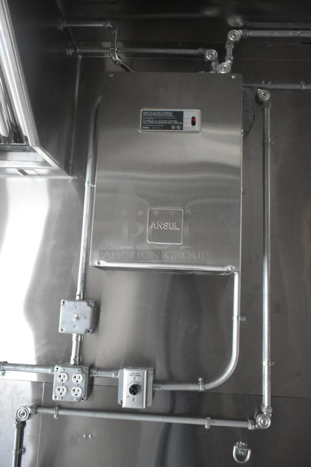 Industrial setup inside a food trailer, featuring an Ansul fire suppression system and electrical outlets. Stainless steel surface.