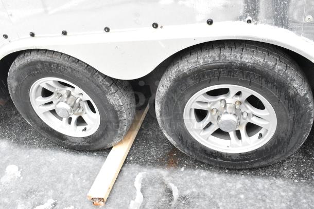 Dual wheels of a 24' Cruising Kitchens food trailer, parked on icy ground, showcasing sturdy tires and silver rims.