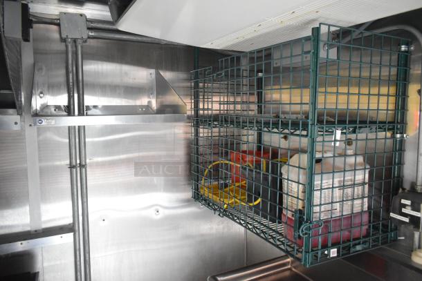Interior of Cruising Kitchens 24' food trailer with stainless steel walls and wire storage rack containing cleaning supplies.