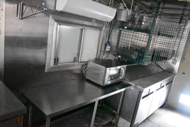 Cruising Kitchens 24' food trailer, stainless steel interior, commercial-grade microwave, shelving, and prep counters.