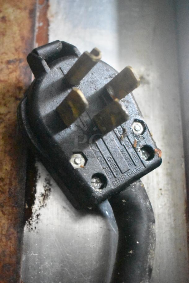 Close-up of a heavy-duty electrical plug, showing metal prongs and visible text indicating voltage and specifications.