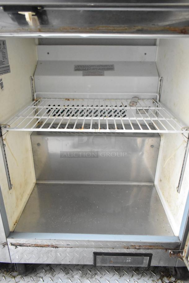 Interior view of Cruising Kitchens food trailer's storage compartment with metal grating and base. Visible wear on edges.