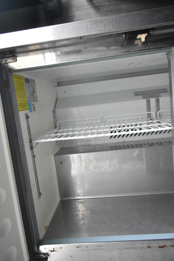 Interior view of a Cruising Kitchens food trailer showing a clean, white, commercial-grade refrigerator with adjustable wire shelving and visible compliance labels.
