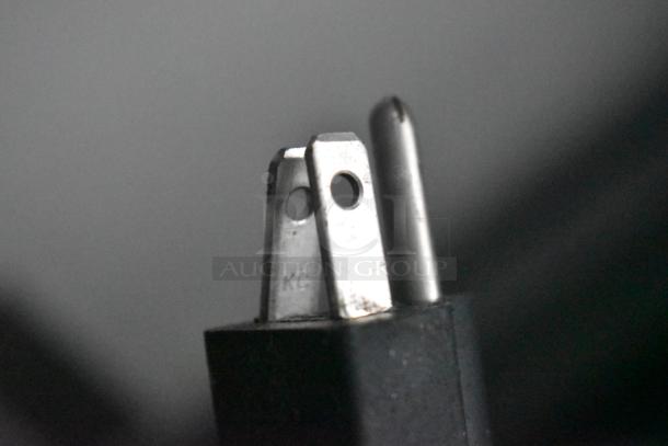 Close-up shot of a power plug with metallic prongs, one marked "KC."