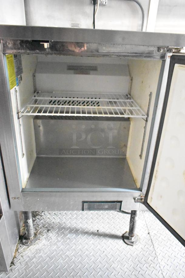 Interior view of Cruising Kitchens 24' food trailer showing a commercial fridge with open door, wire shelves, and metal interior.