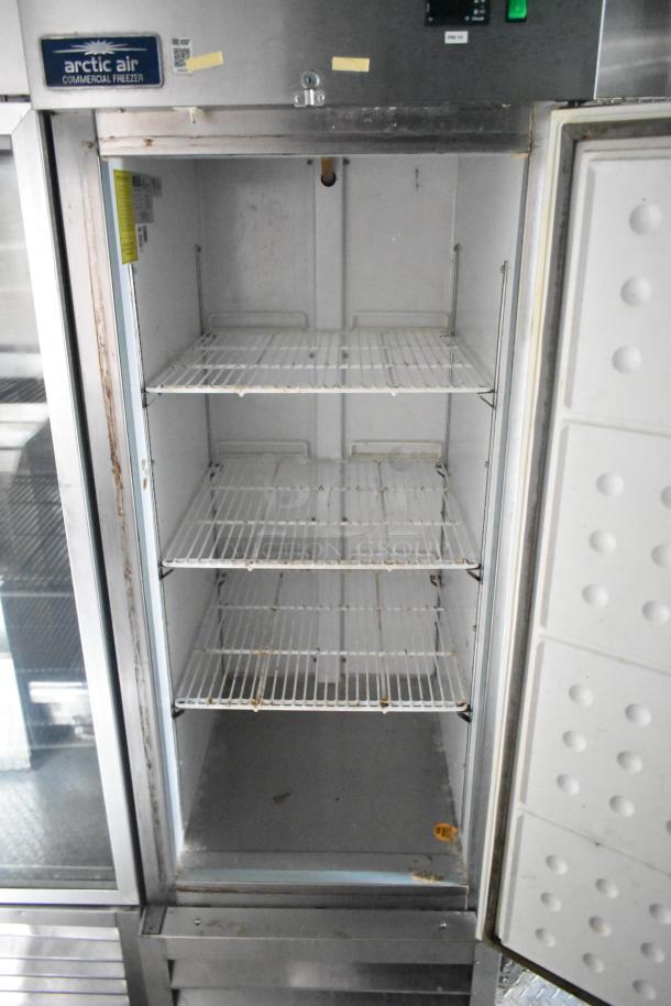 Arctic Air commercial freezer with open door, showcasing four wire shelves. Some visible wear inside. Plaque reads "Arctic Air."