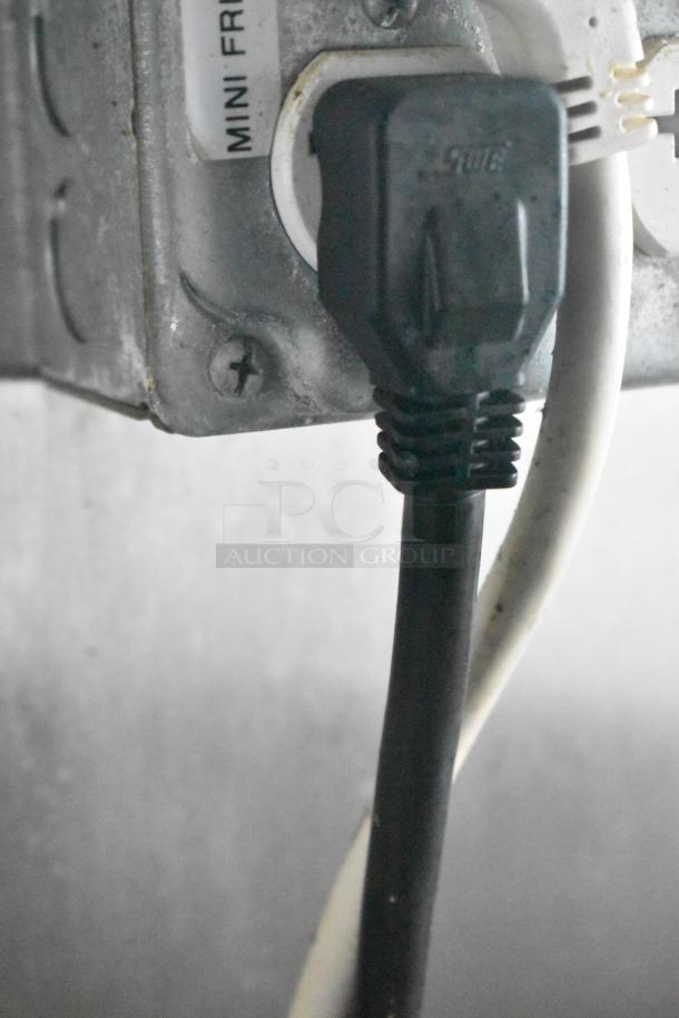 Close-up of a power plug labeled "MINI FRIDGE," connected in a Cruising Kitchens food trailer.