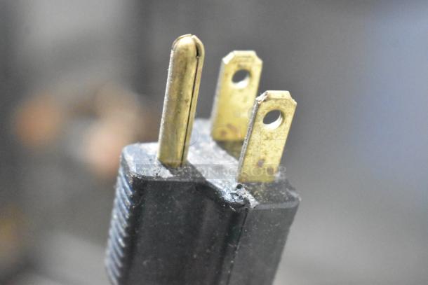 Close-up of a three-prong plug, showing metal prongs and black plastic casing. Part of the Duke convection oven auction item.
