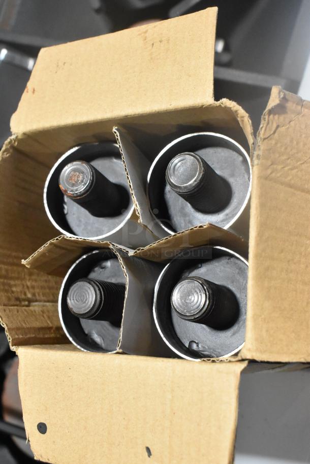 Top view of a cardboard box containing four black metal components, possibly range knobs, in divided sections.