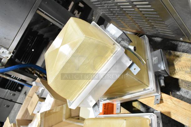 Pallet of various light fixtures with metallic frames and textured glass covers, including an emergency light. Displayed on wooden pallet.