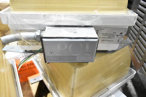 Pallet lot of various light fixtures, including emergency light; features metal casing, plastic lens, new condition.