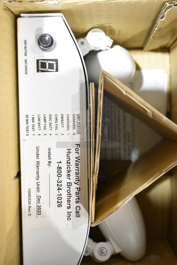 Pallet of light fixtures including emergency light with test button. Warranty info: Hunzicker Brothers Inc, valid until Dec 2023.