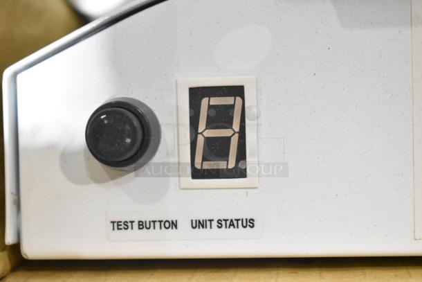 Emergency light fixture with digital display and test button. Markings indicate "Test Button" and "Unit Status."