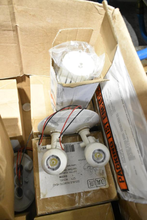 Pallet of various light fixtures, including emergency lights. Visible Dual-Lite remote head model in box. Items appear new.
