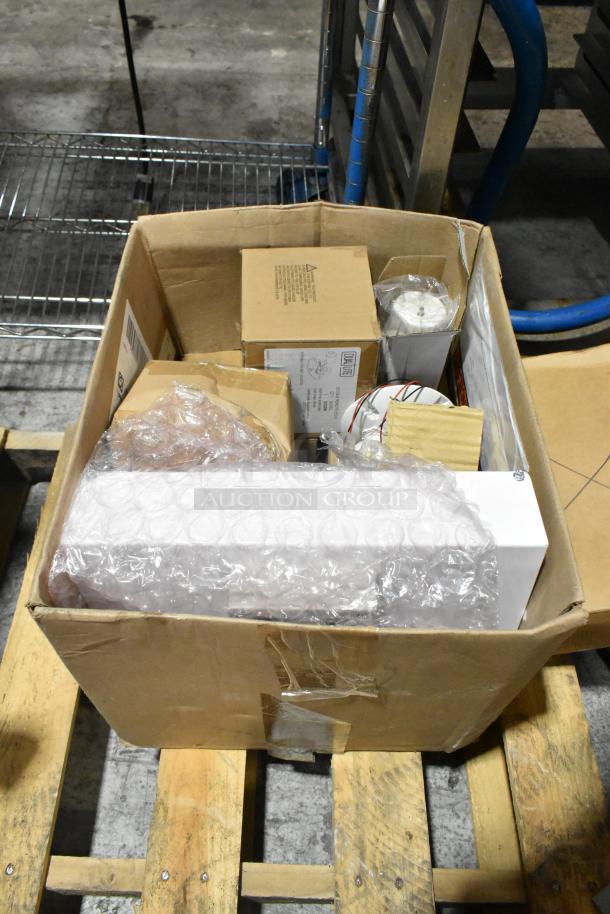A boxed pallet lot of various light fixtures including an emergency light, visible packaging, and labels indicating mixed items.