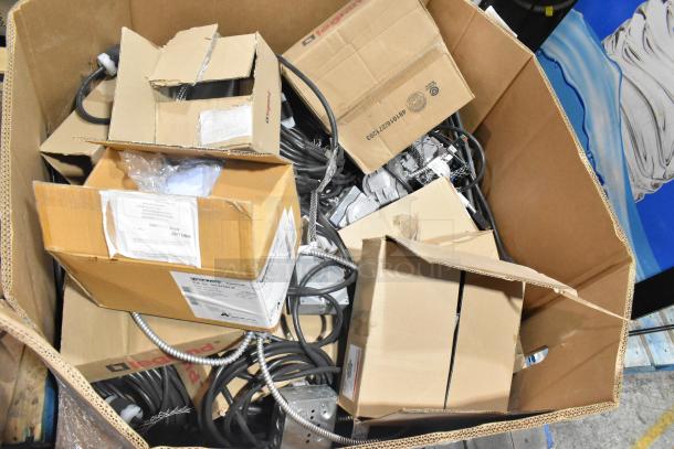 A large pallet with various boxed items including Critical Cover AquaTank shoe covers, wires, and Wiremold CDBB1420C-40BK CD with outlet box. Boxes show wear and labels.