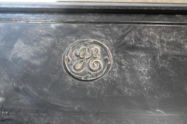 Pallet lot including GE outdoor light fixtures, black surface with embossed "GE" logo, dusty condition.