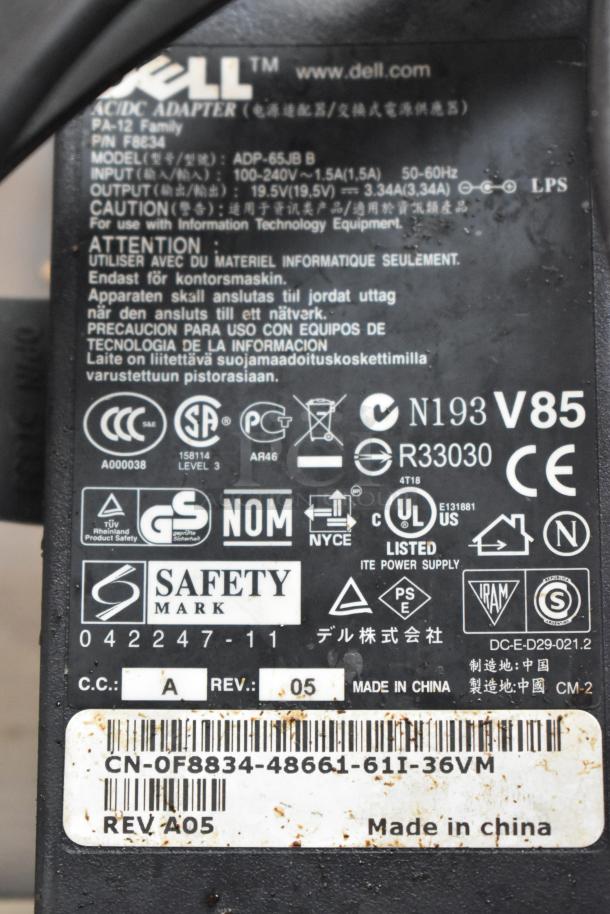 Close-up of a Dell Inspiron 15R-5537 charger label, model ADP-65JB B, showing input/output specifications and safety marks.